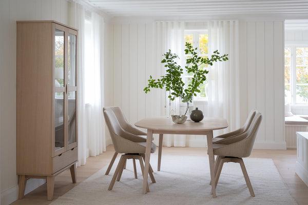 Ljus matplats med runt matbord, fyra stolar och vitrinskåp i ljust trä med naturlig skandinavisk stil