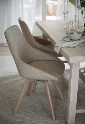 Moderna matstolar i beige tyg med träben vid matbord i ljus skandinavisk matsal