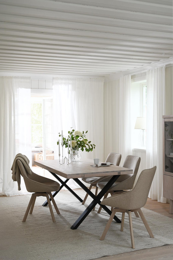 Matbord med kryss i metall och träskiva, omgivet av fyra beige stolar i ljust matrum med vita väggar