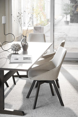 Moderna matstolar med beige tyg och svarta ben vid matbord i ljust skandinaviskt hem