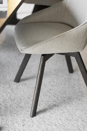 Grå matstol med svarta träben i närbild, visar kurvad rygg och sits i ljusgrått tyg på vit matta