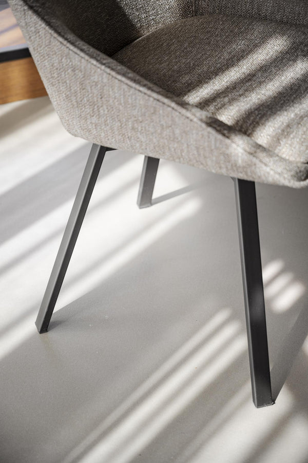 Närbild på grå fåtölj med svarta metallben och elegant design på vitt golv