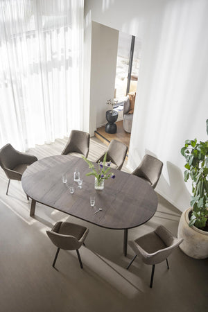 Oval matbord i mörkgrått med sex stoppade stolar i taupe runt bordet, ovanifrån i ljust matrum