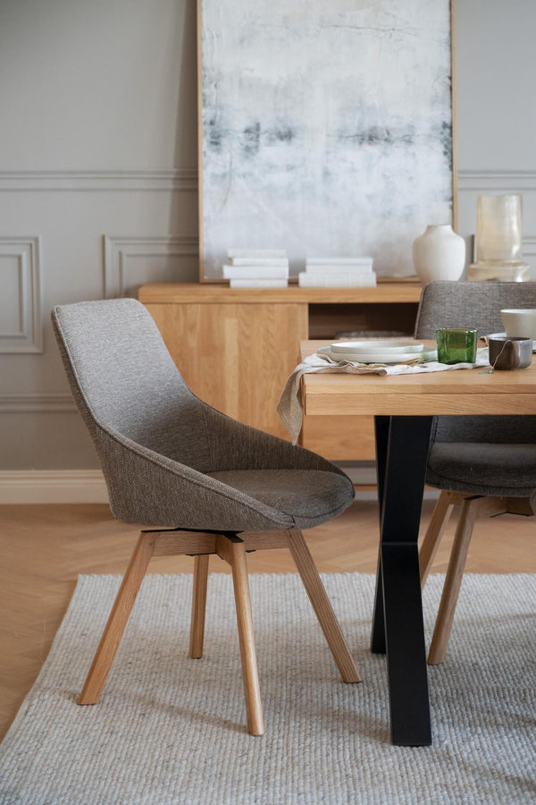 Grå stoppad stol med träben vid matbord i modern skandinavisk matsal med ljust trägolv