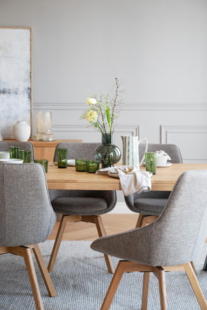 Matbord i ek med gråa stolar och grön glasdekor i skandinavisk matsal
