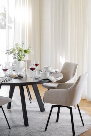 Matbord med svarta ben och grå stolar i elegant matsal med vita gardiner och dukat bord