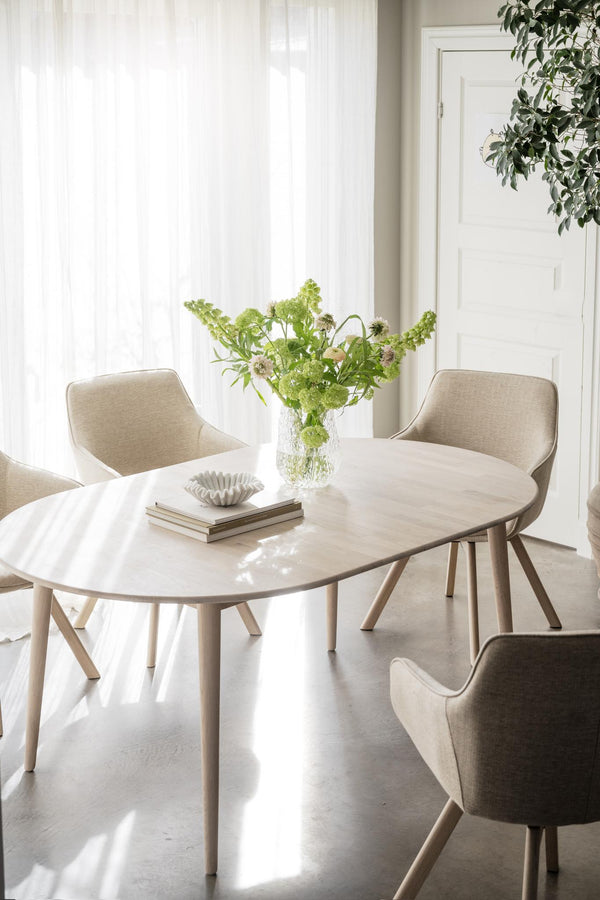 Runt matbord i ljust trä med moderna stolar och vas med gröna blommor i skandinavisk matsal