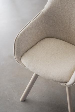 Närbild på beige fåtölj med mjuk klädsel och trälånga ben, elegant skandinavisk design