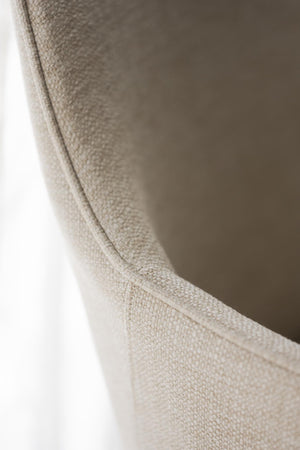 Närbild på beige fåtölj med textilfärgad klädsel och synlig söm längs kanten