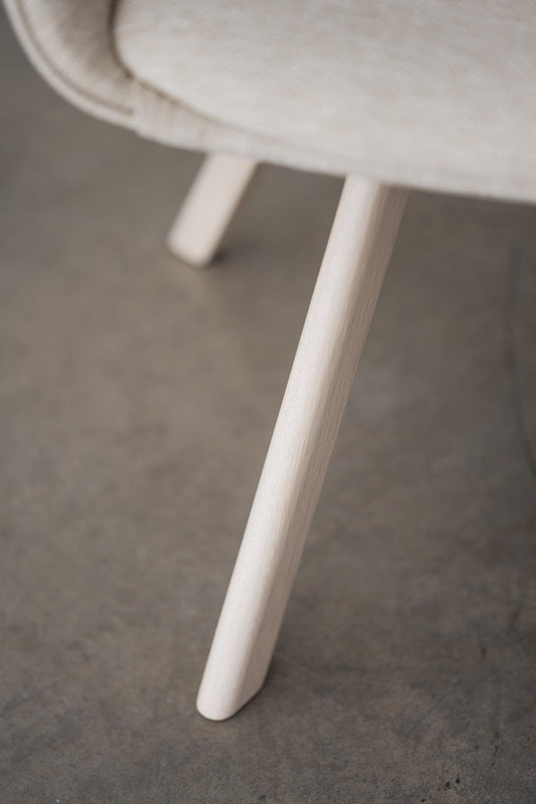 Närbild på vit stolsben i massivt trä med rundad design och naturlig trästruktur mot grått golv