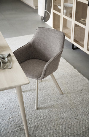 Grå stol med armstöd och ljusa träben vid matbord i skandinavisk inredning