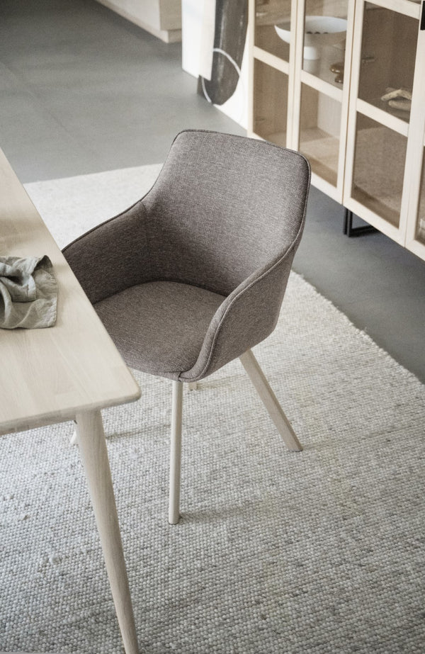 Grå stol med armstöd och ljusa träben vid matbord i skandinavisk inredning