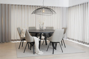 Rund matgrupp i svart med sex ljusgrå stolar och wirelampa i modern matsal med vita gardiner
