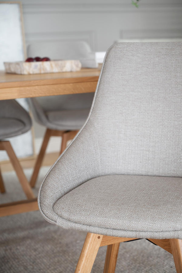 Grå matstol med stoppad sits och rygg i tyg samt ljusa träben vid matbord i modern skandinavisk stil