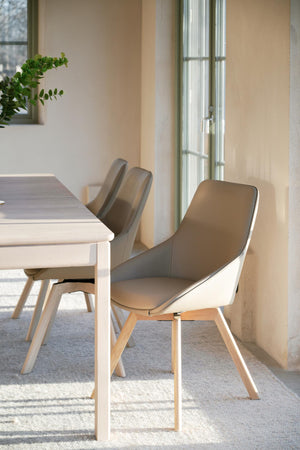 Moderna matstolar i beige läder med träben vid matbord i ljust skandinaviskt kök