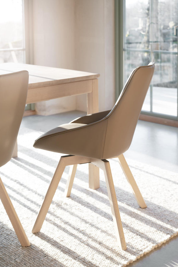 Beige matstol med träben i ljust trä vid matbord i modern skandinavisk stil