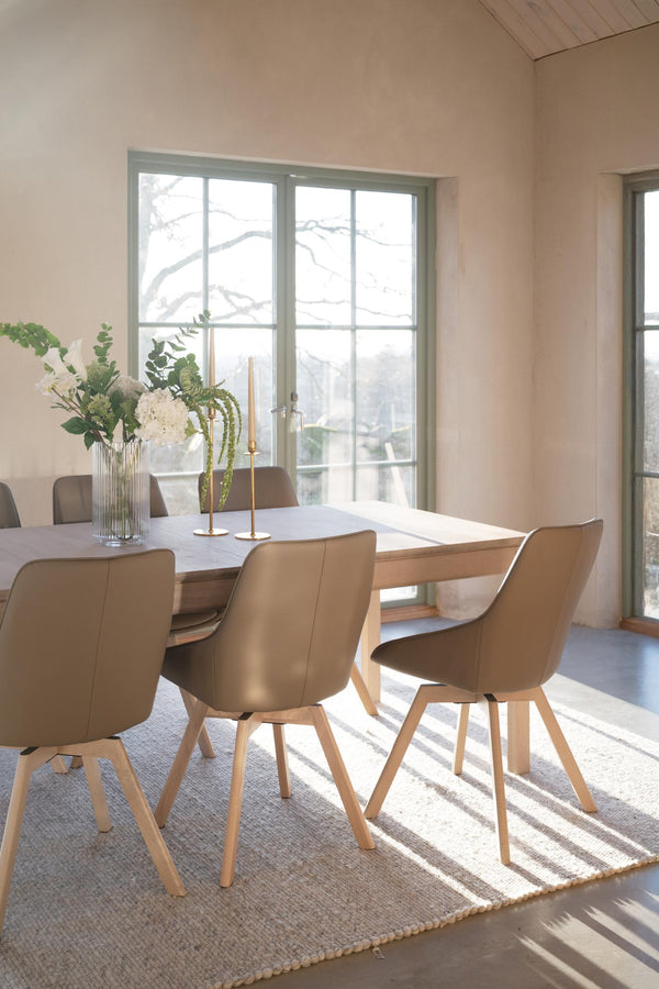 Matbord i trä med beiga stolar i modern matsal med stora fönster och naturligt ljus