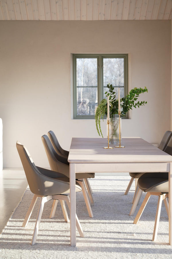 Matbord i ljust trä med moderna stolar i grått och beige, glasvas med gröna växter som dekoration