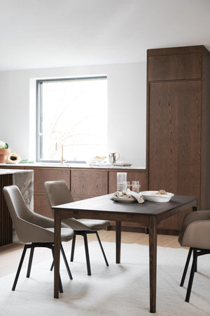 Matbord i mörkt trä med taupefärgade stolar i modernt kök med matchande skåp och högt skåp
