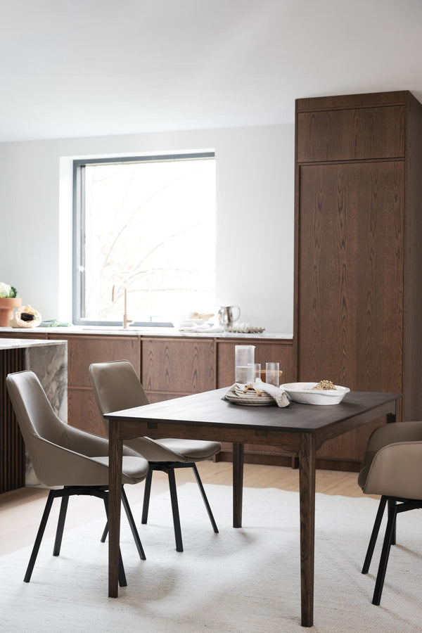 Matbord i mörkt trä med taupefärgade stolar i modernt kök med matchande skåp och högt skåp