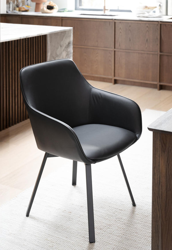Svart stol med armstöd och metallben i modern köksmiljö med träskåp