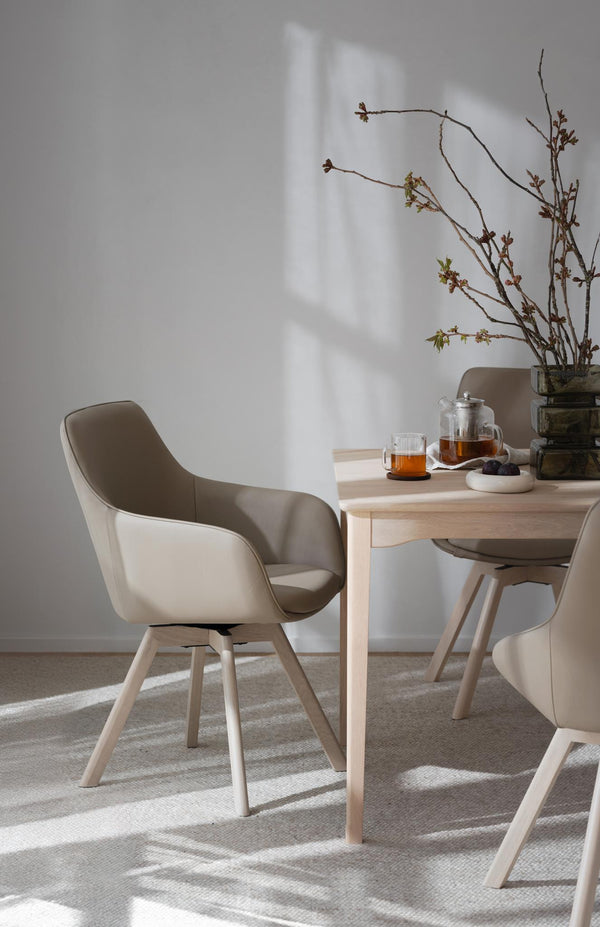 Beige matstol med träben vid matbord i ljust rum med teservis och vårgrenar i vas