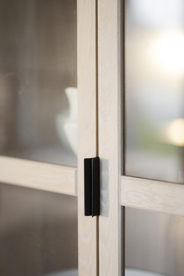 Minimalistiskt svart möbelhandtag monterat på ljus träskåpsdörr med glasdetaljer