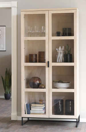 Vitrinskåp i ljust trä med glasdörrar, metallställning och inredning av glas, keramik och böcker