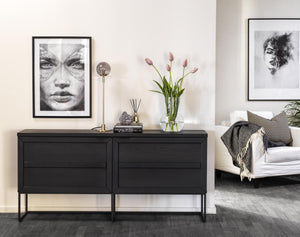 Svart sängbord med lådor och metallben i modernt sovrum med tavlor och tulpaner