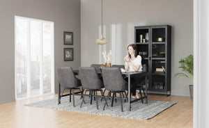 Matgrupp med grå stolar och svart skåp i modern matsal med kvinna som dricker kaffe