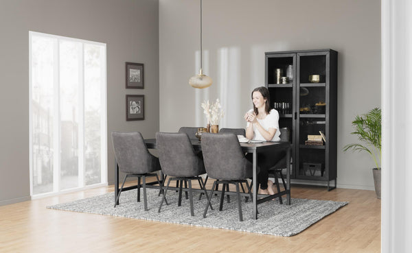 Matgrupp med grå stolar och svart skåp i modern matsal med kvinna som dricker kaffe