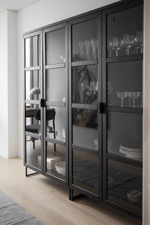 Modernt skåp med glaspridedörrar i svart ram, fyllt med glas, tallrikar och servis i minimalistisk inredning