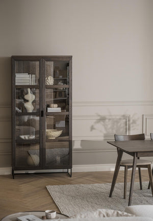 Vitrinskåp i mörkt trä med glashyllor och synliga föremål i elegant matsal med bord och stolar