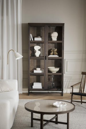 Mörkt vitrinskåp med glaspaneler, dekorerat med vita skulpturer, böcker och keramik i modernt vardagsrum