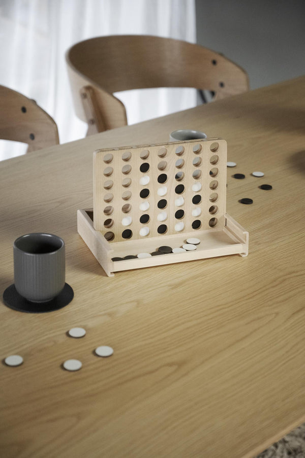 Fyra i rad spel i trä med naturligt ljus trä, svarta och vita brickor på runt matbord med stolar