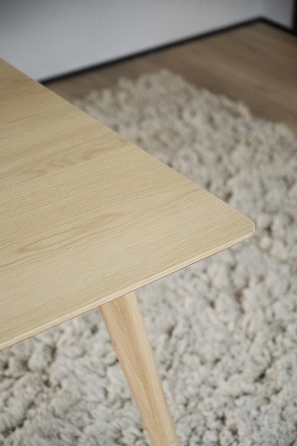 Närbild på ljust träbord med synlig trästruktur och ben, placerat på grå luggmatta i modern inredning