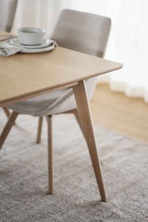 Ljust träbord i ek med skandinavisk design, rundade ben och minimalistisk stil, med kopp och stol i bakgrunden