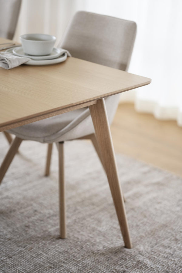 Ljust träbord i ek med skandinavisk design, rundade ben och minimalistisk stil, med kopp och stol i bakgrunden