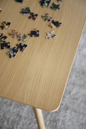 Pusselbitarna ligger utspridda på träbord med ekfanér och rundade hörn