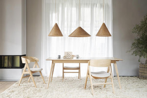 Matbord i ljust trä med tre stolar och flätade taklampor i skandinavisk stil över vit matta