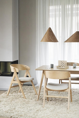 Matbord i ljust trä med matchande stolar och beige kuddor på luddig matta i skandinavisk stil