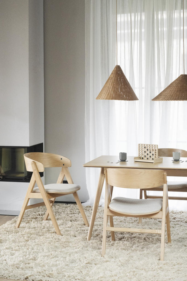 Matbord i ljust trä med matchande stolar och beige kuddor på luddig matta i skandinavisk stil