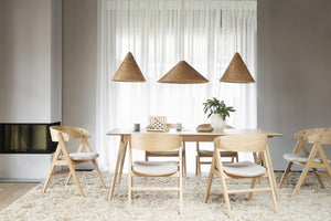 Ljus matplats med träbord, stolar i ljust trä och flätade lampor över vita gardiner