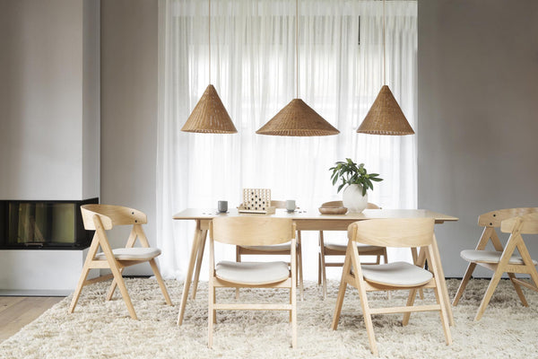 Ljus matplats med träbord, stolar i ljust trä och flätade lampor över vita gardiner