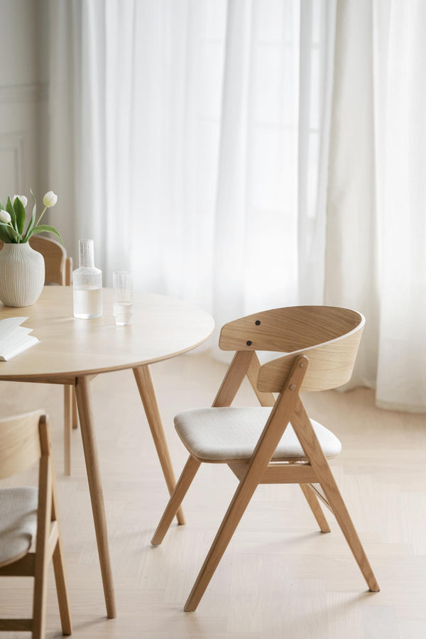 Skandinavisk matstol i ljust trä med vit stoppning vid runt matbord i minimalistisk matsal