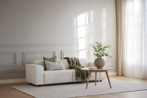 Ljus vardagsrumsinredning med beige soffa, tresidobord i trä och gröna textildetaljer vid fönster