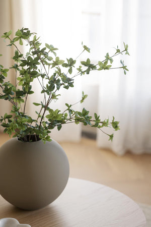 Konstgjorda gröna kvistar i grå rund vas på träbord i ljust skandinaviskt rum