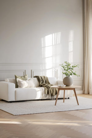 Ljust vardagsrum med vit soffa, beige pläd, runt soffbord i trä och grön växt i vas