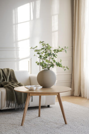 Runt soffbord i ljust trä med grön växt i sfärisk vas, skandinavisk inredningsstil