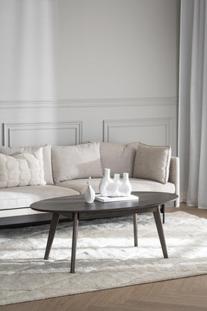 Oval soffbord i mörkt trä med vita vaser i elegant vardagsrum med beige soffa och ljus matta